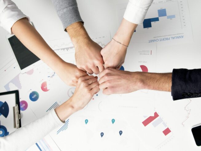 Free Colleagues celebrate success with a fist bump over financial charts depicting teamwork and unity. Stock Photo