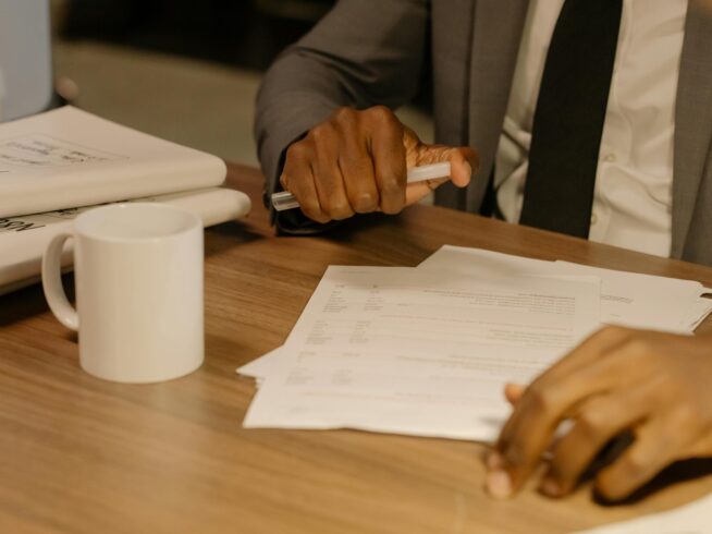 Free Close-up of a businessman holding and reviewing documents on a wooden desk. Stock Photo
