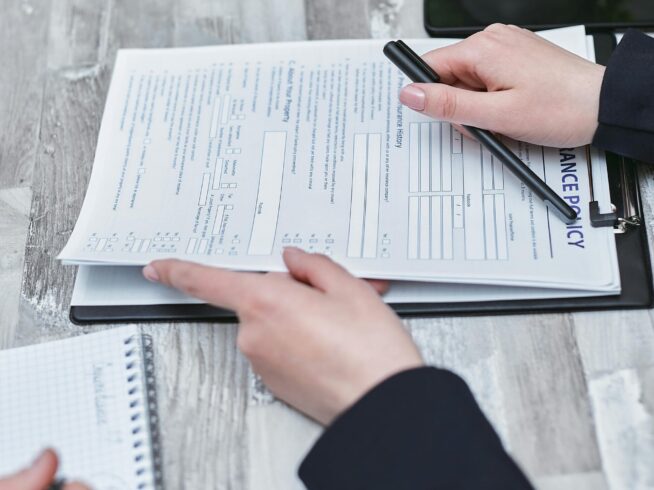 Free Close-up of hands analyzing insurance policy paperwork with pen on table. Stock Photo